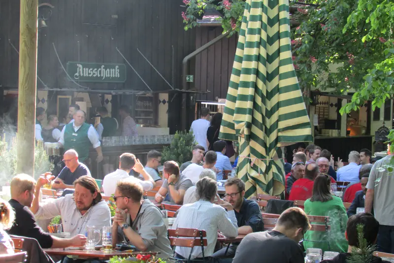 Guests at long tables under the chestnut trees, with the Ausschank serving hut, at the Augustiner-Keller beer garden in Munich